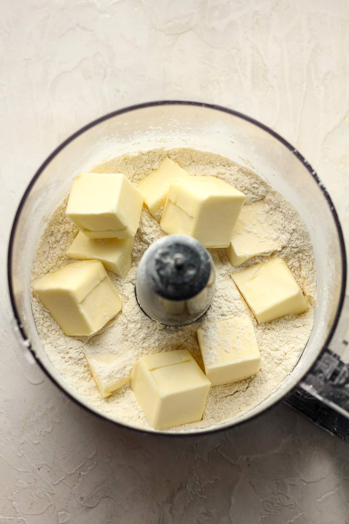 A food processor of the pie crust ingredients showing chunks of butter.