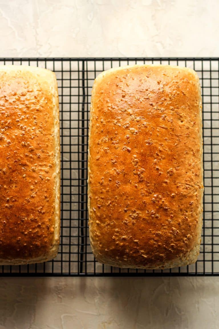 A wire rack with two loaves of homemade cracked wheat bread.