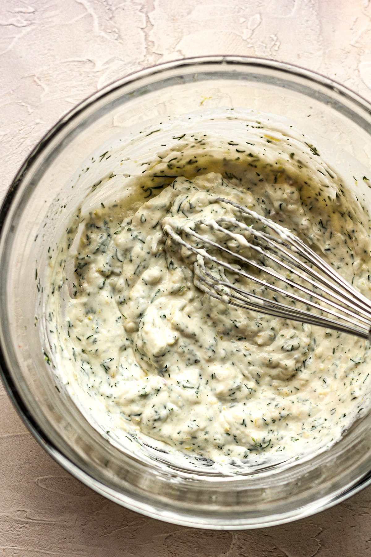 A bowl of the combined ingredients for the lemon dill sauce and a whisk inside.