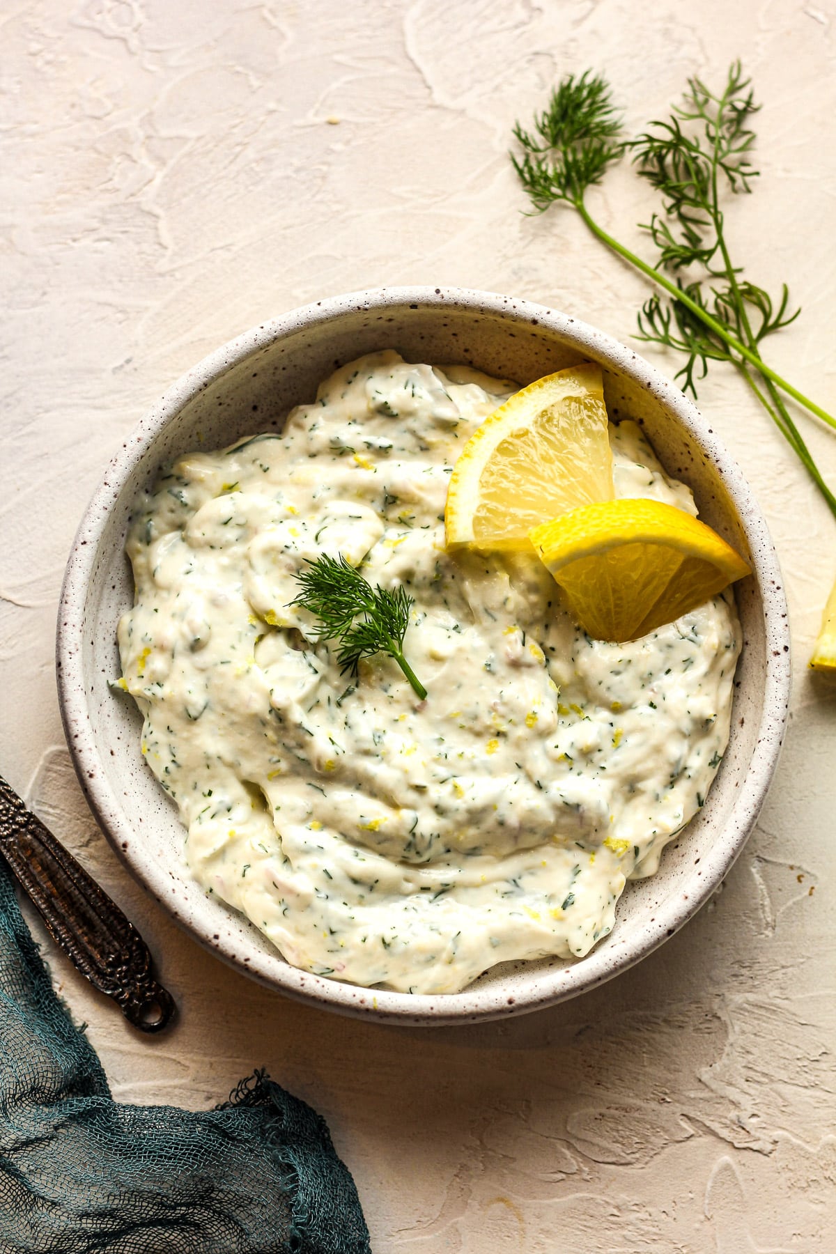 A bowl of dill sauce with lemon on a white surface.
