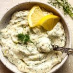 Closeup on a bowl of the lemon dill sauce with lemon slices on top.