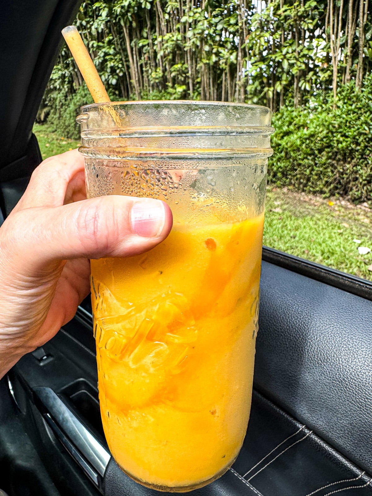 Side view of my hand holding a mango smoothie.