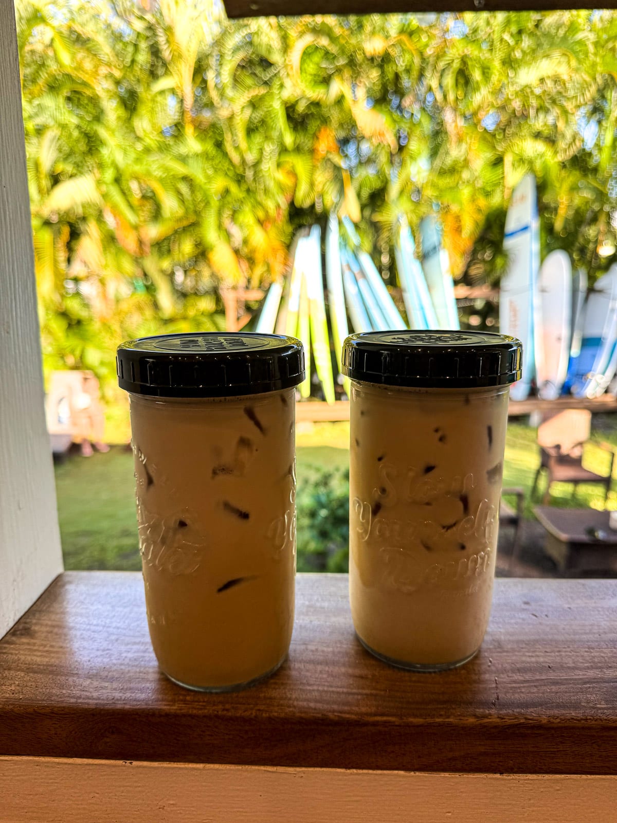 Side view of two iced coffees in front of palm trees and surf boards.
