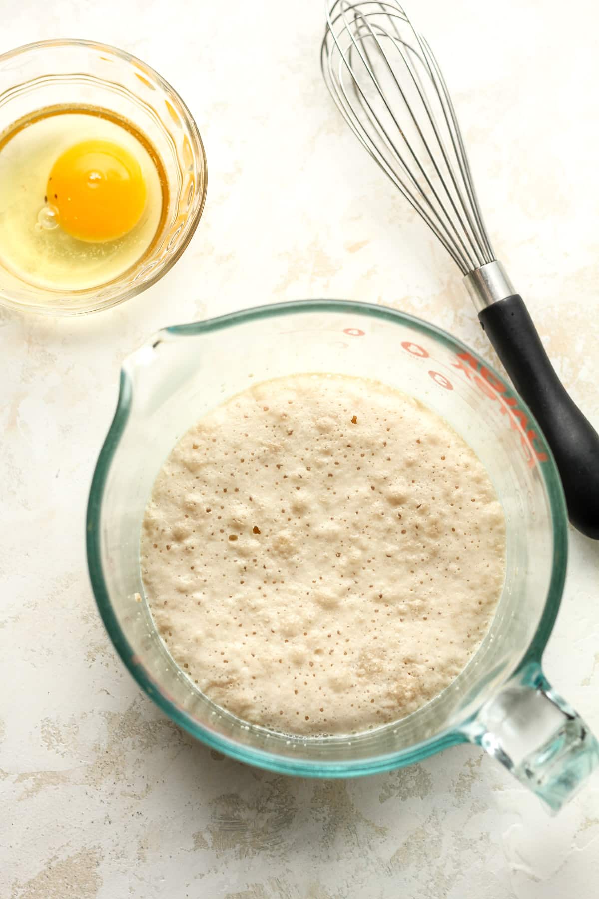 A measuring cup of the yeast mixture and a small bowl with an egg.