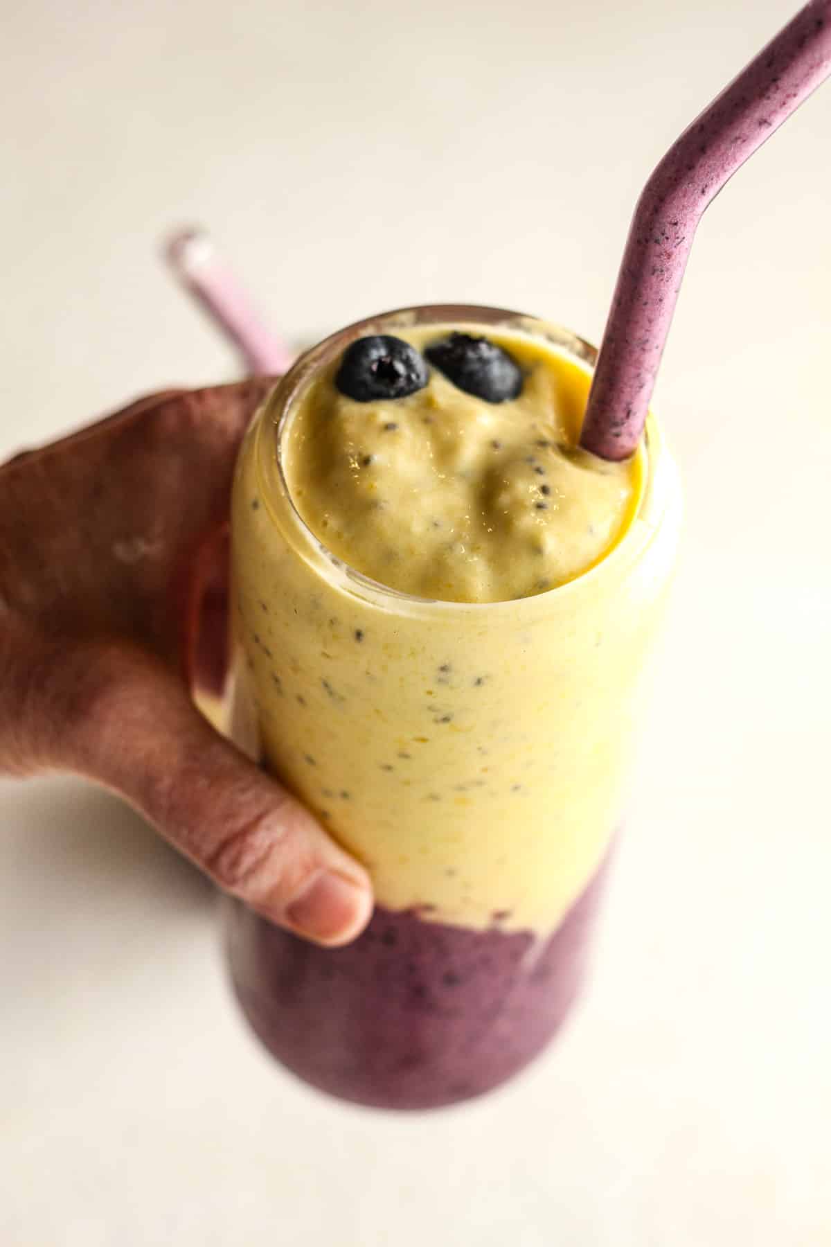 A hand holding a blueberry mango smoothie with chia seeds.