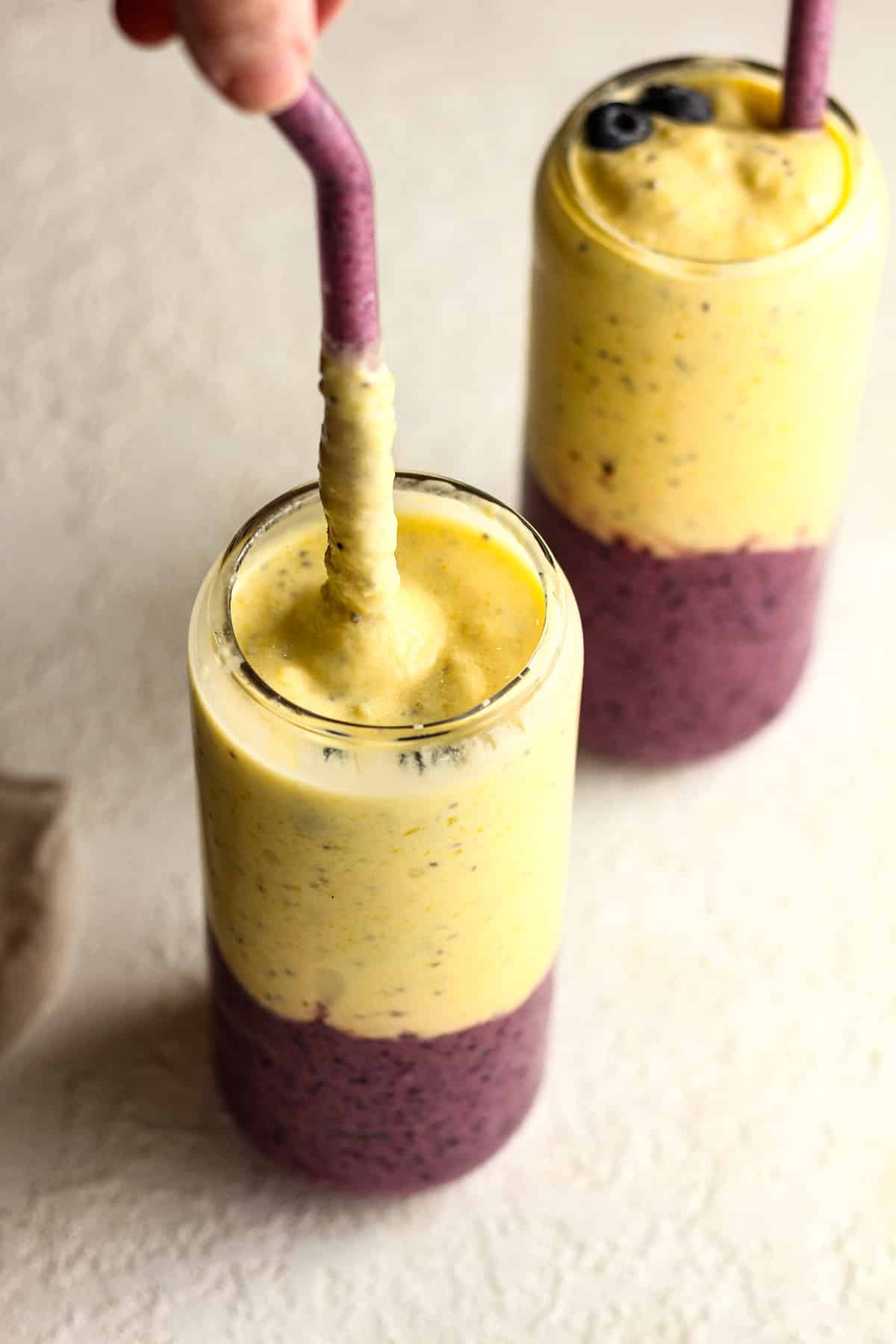 Overhead view of two layered fruit smoothies with a hand pulling one of the straws upward.