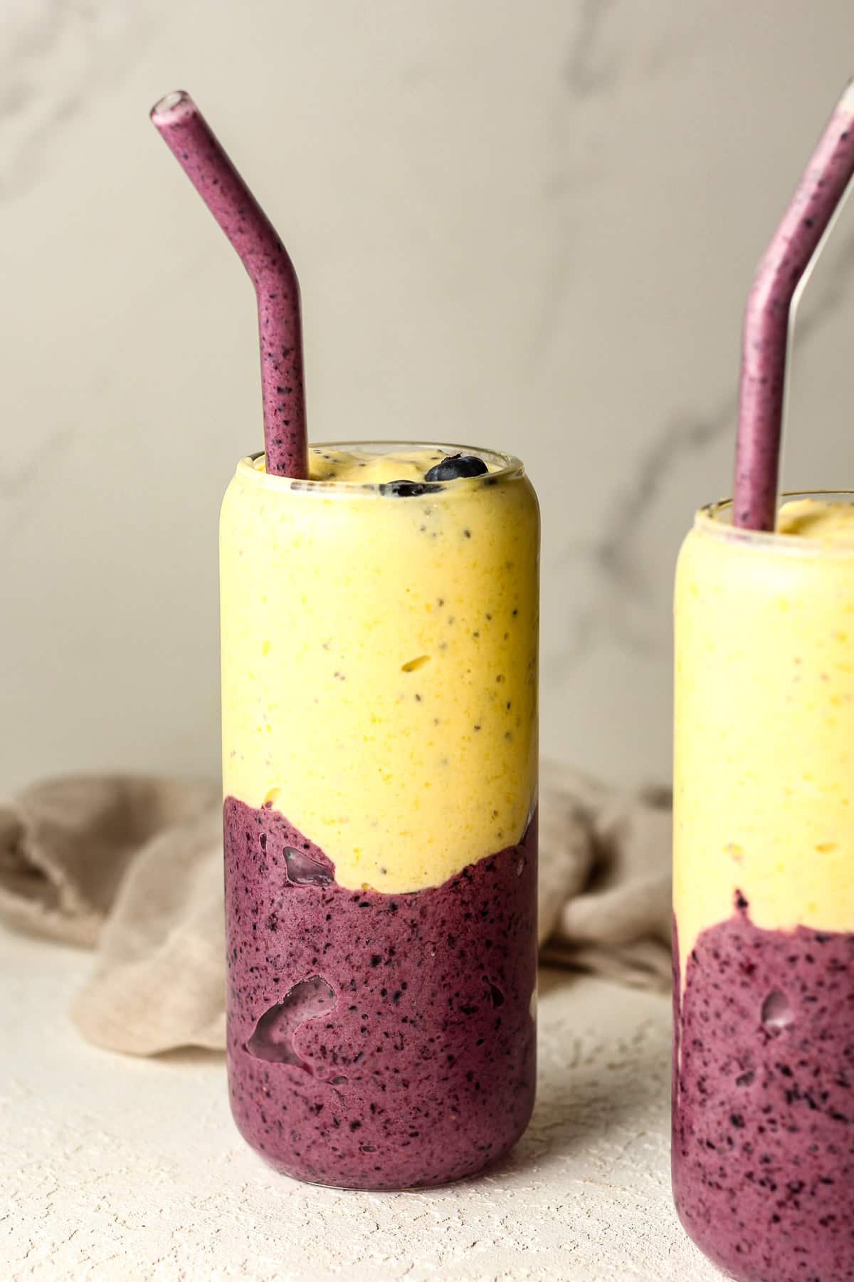 Side view of blueberry mango smoothies with glass straws.