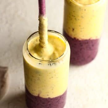 Side view of two blueberry mango smoothies with glass straws.