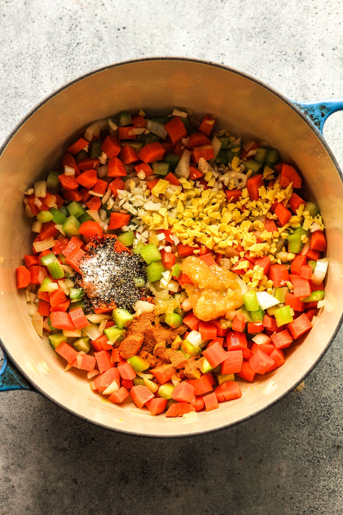 A pot with sauteed veggies topped with minced garlic, ginger, lemon paste, and seasonings including salt, pepper, and turmeric.