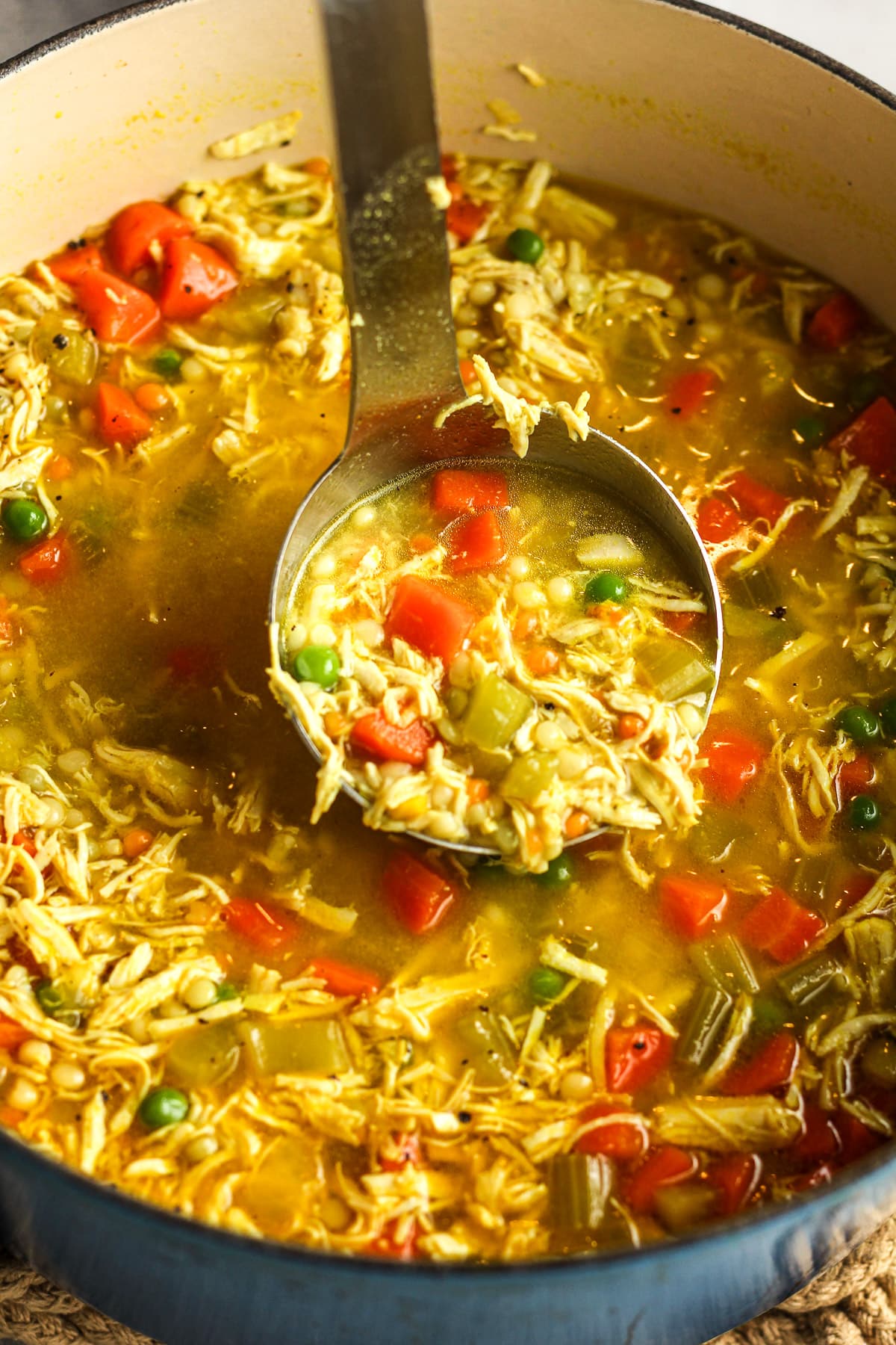 Side view of a pot of chicken and couscous soup with a soup ladle pulling some upward.