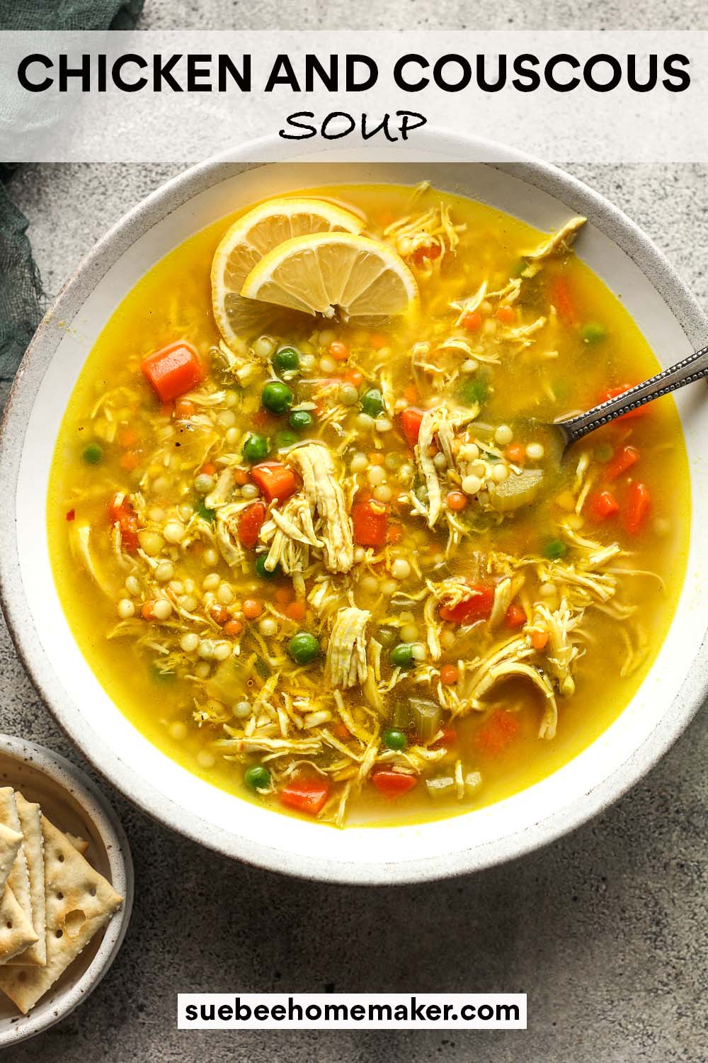 A shallow bowl of chicken and couscous soup with a spoon and lemon slices.