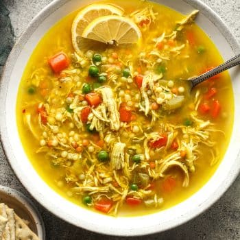 Closeup on a bowl of chicken and couscous soup with a spoon.