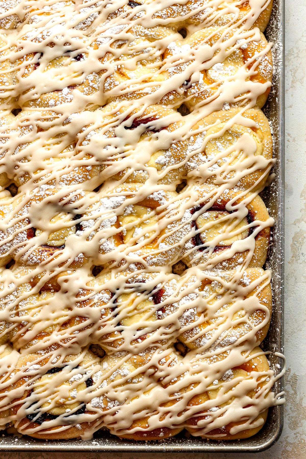 A pan of fruit-filled cream cheese kolaches with a drizzle of icing.