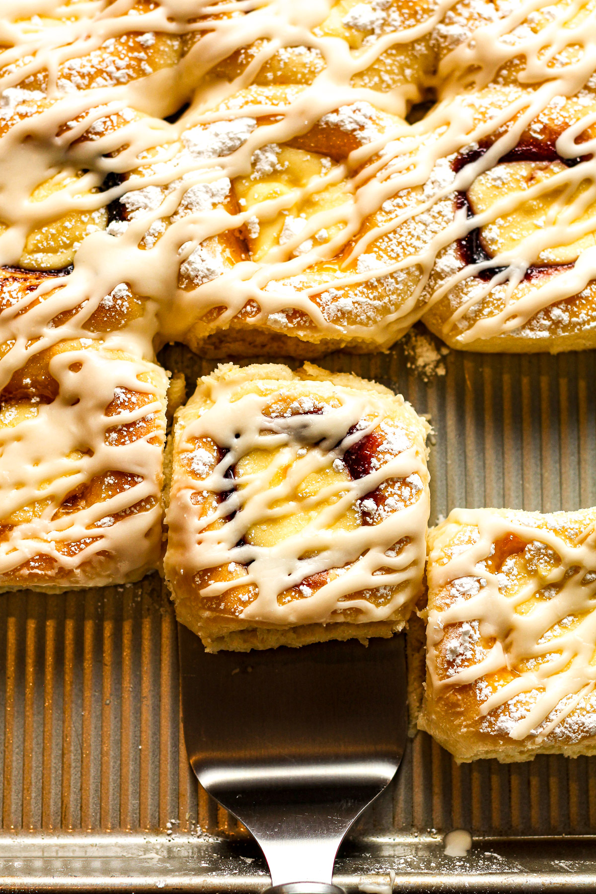 Overhead view of a spatula under a fruit filled kolache with cream cheese and icing.