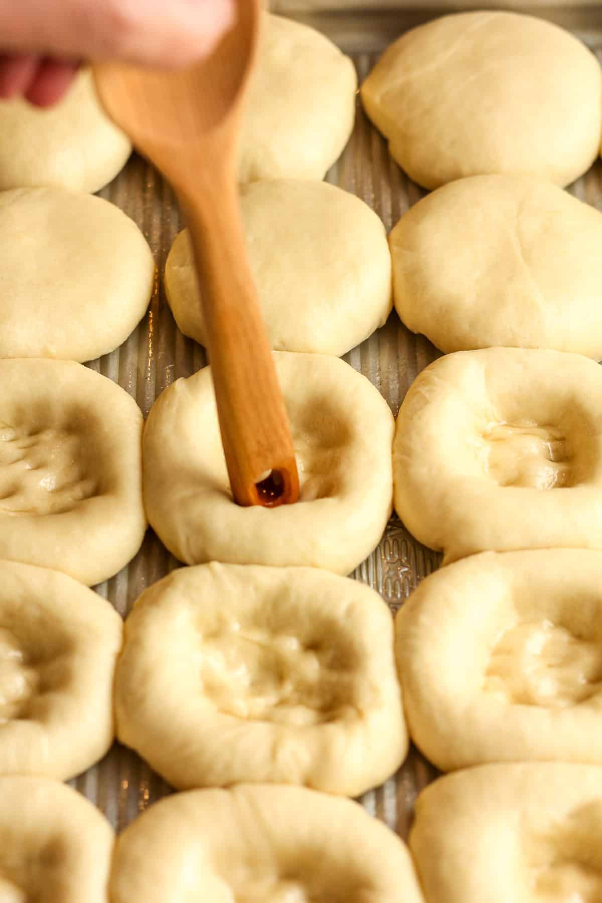 A wooden spoon being pressed into the middle of the kolache rolls.