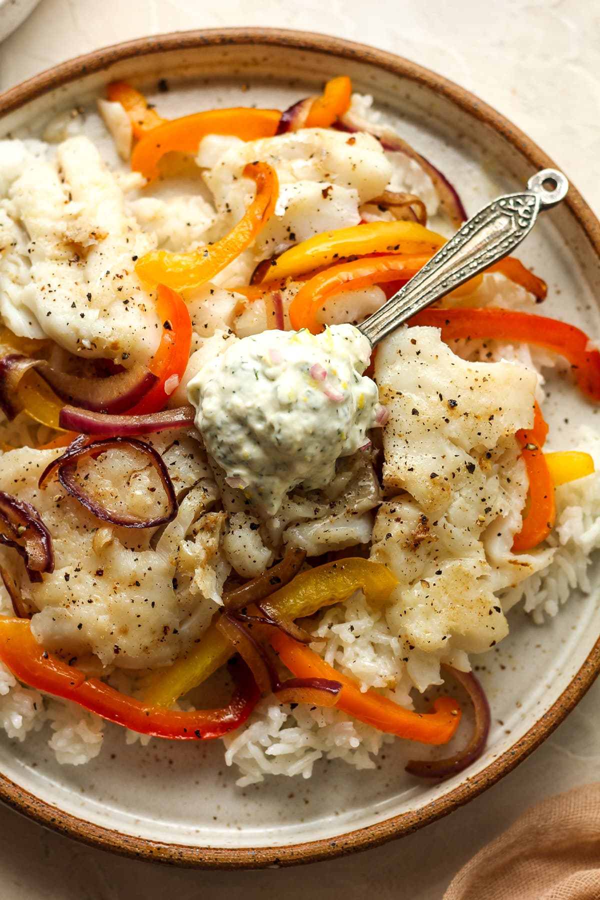 A plate of fish over rice and veggies with a dollop of lemon dill sauce.