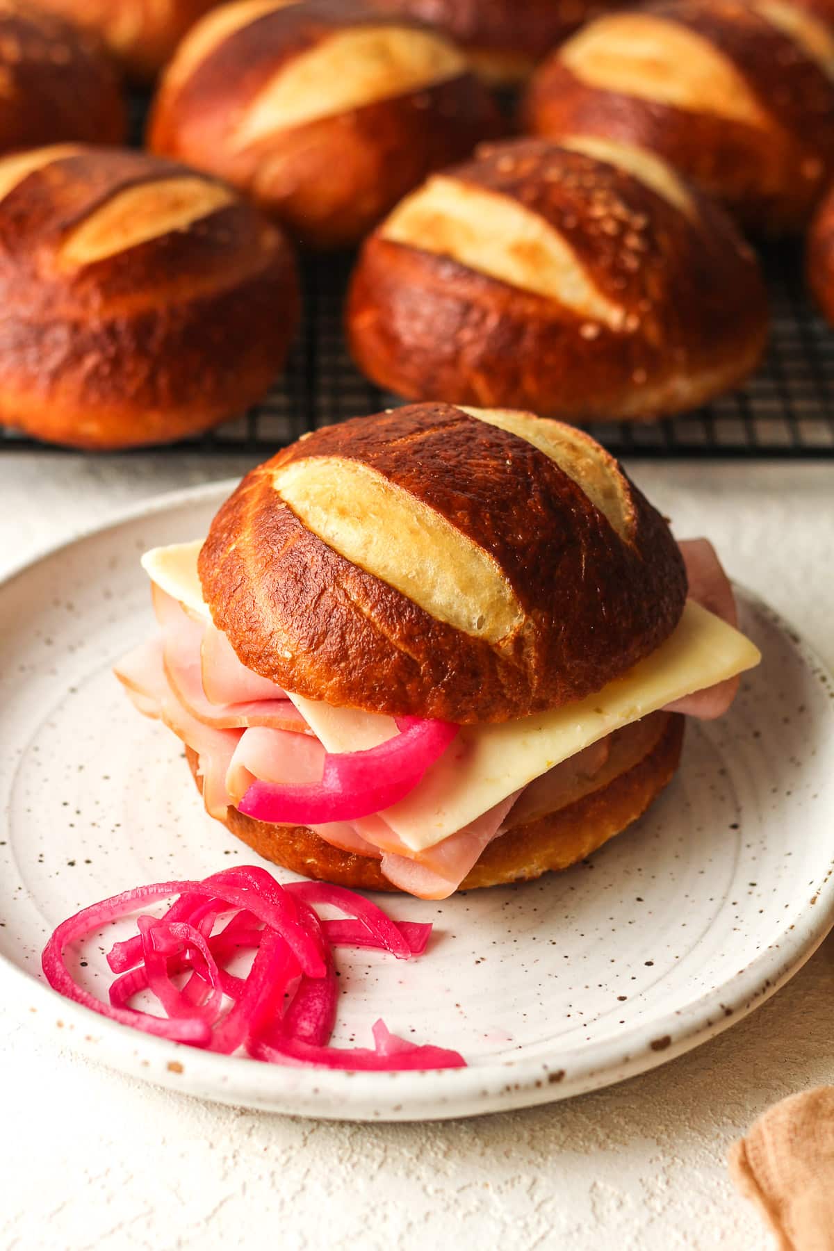 Side view of a plate with a pretzel bun sandwich with pickled red onions.