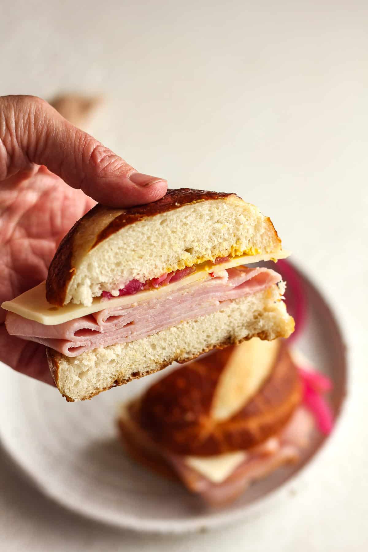 Side view of a hand holding half of a sandwich in a pretzel bun.