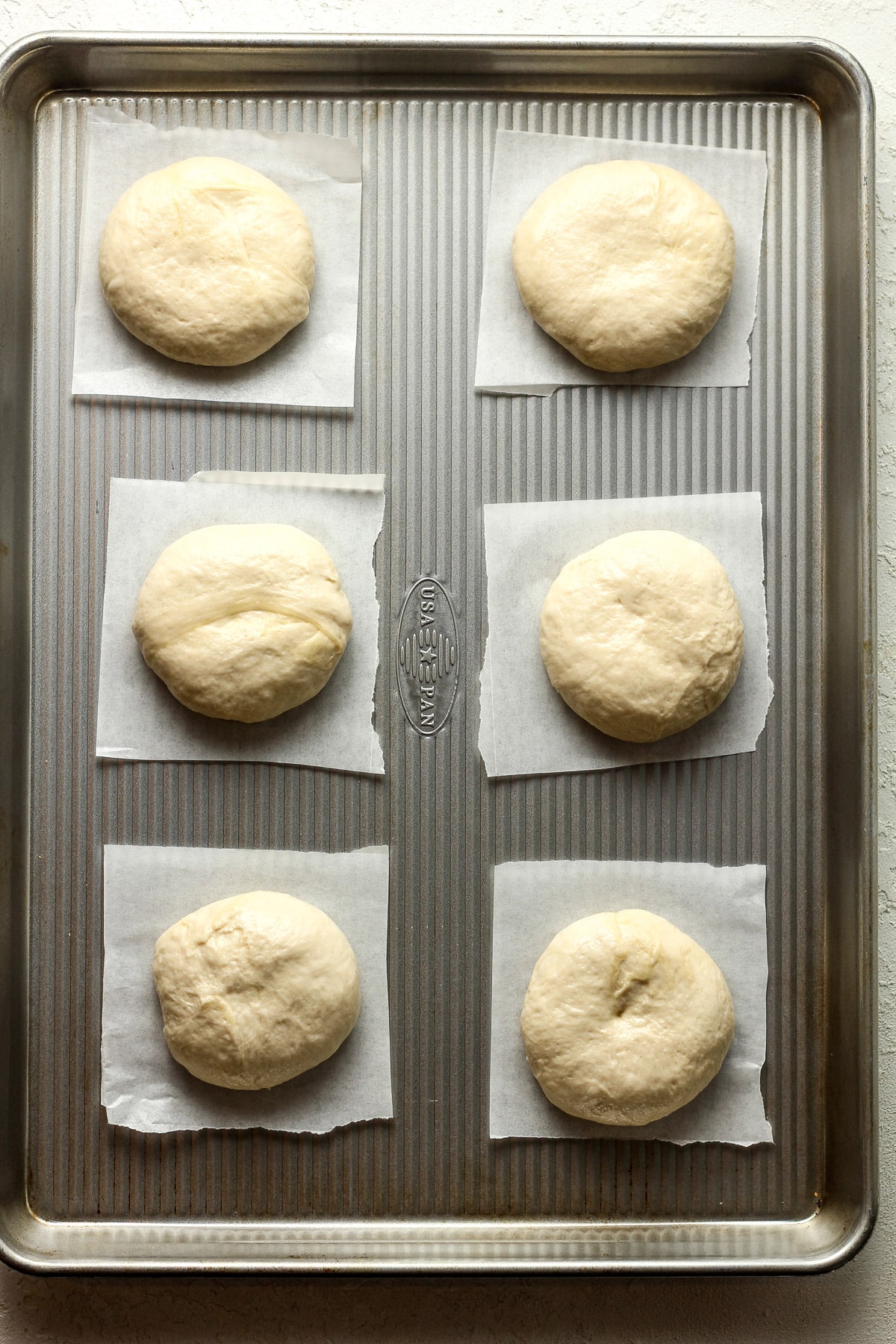 A pan with six rounds of dough on individual squares of parchment paper.