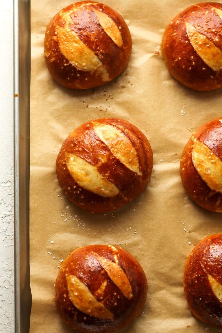 Six pretzel buns on a pan with parchment paper.