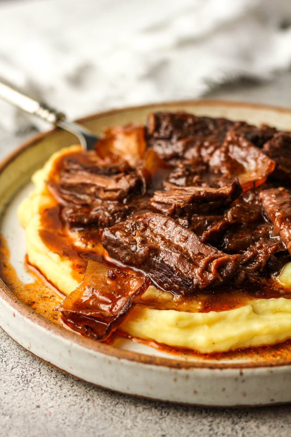 Side view of a plate of mashed potatoes with braised pot roast.