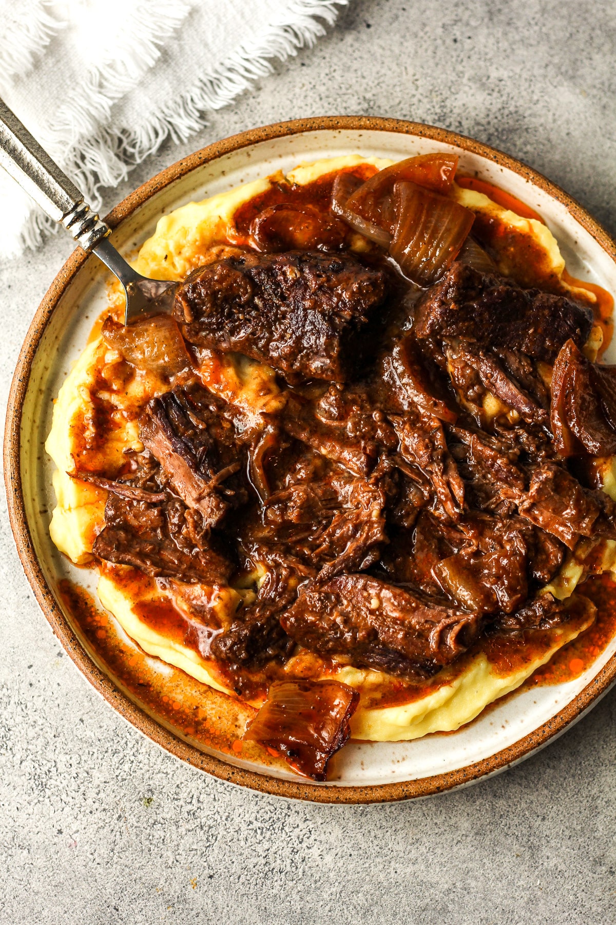 A plate of mashed potatoes topped with braised beef and onions.