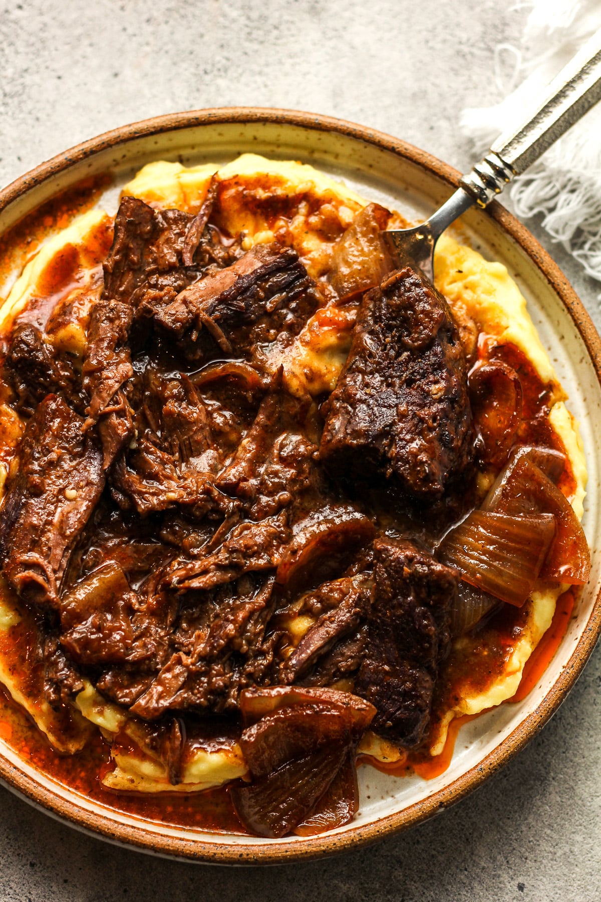 A shallow plate of red wine braised pot roast over mashed potatoes.