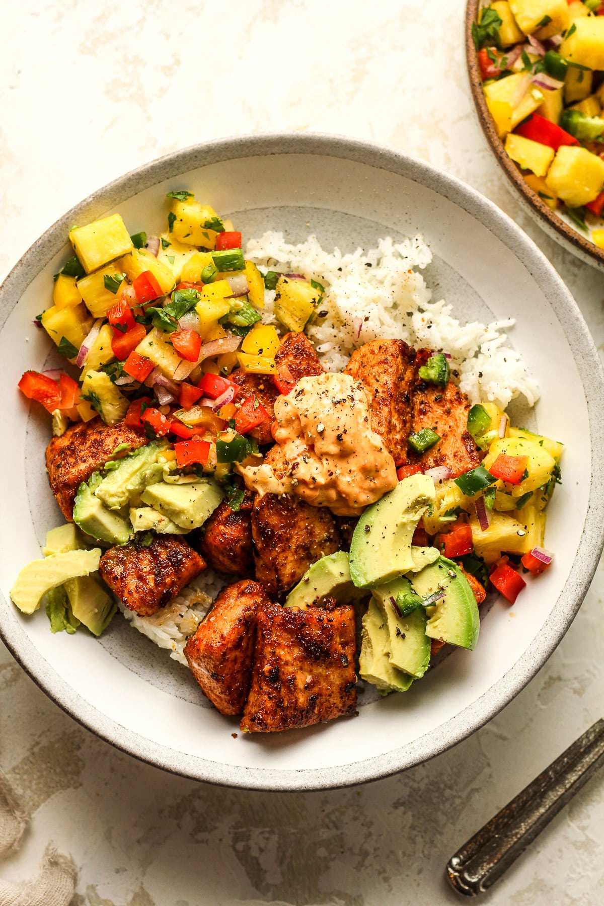 A blackened salmon rice. bowl with a bowl of pineapple salsa next to it.
