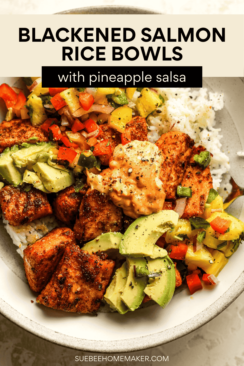 Overhead shot of a rice bowl with blackened salmon bites, pineapple salsa, sliced avocado, and sriracha mayo.