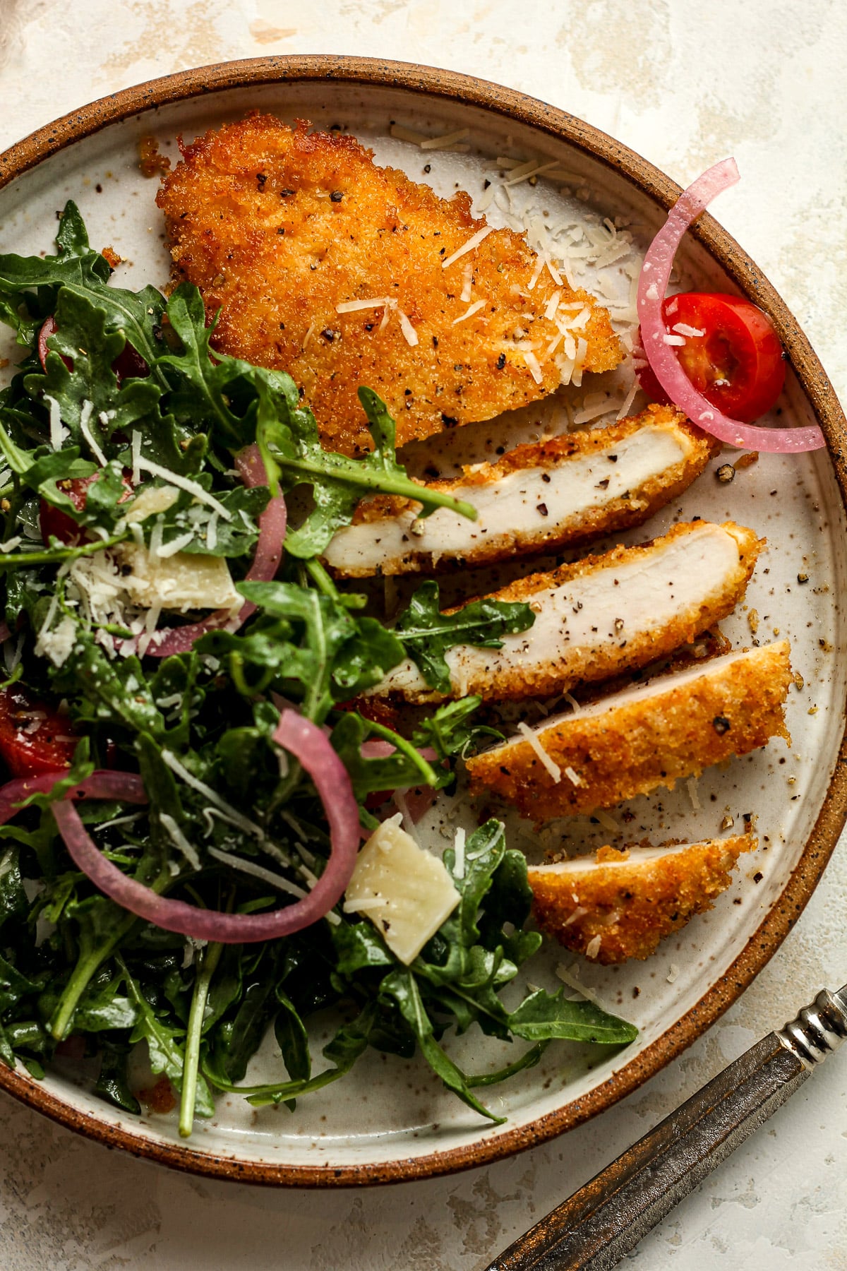 Closeup on a plate with a panko crusted chicken cutlet sliced into strips with arugula salad.