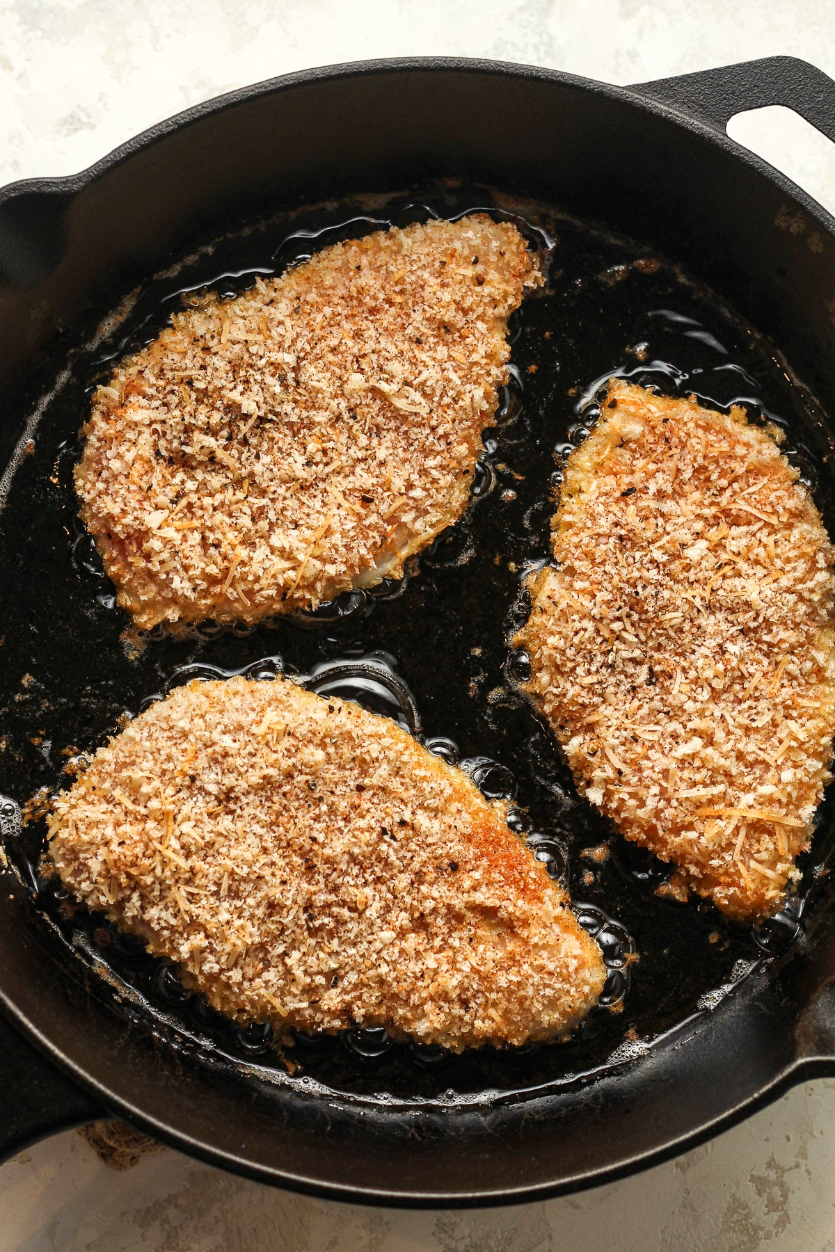 The skillet of the chicken cutlets in avocado oil before flipping.