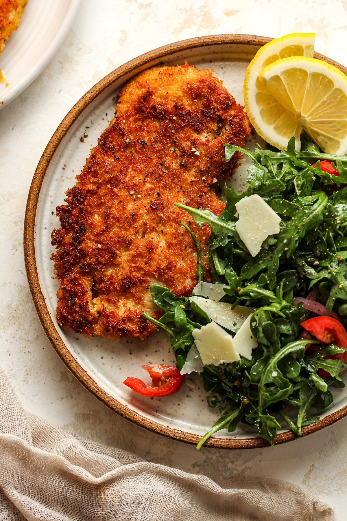 A plate with a chicken cutlet encrusted in panko and parmesan plus arugula.