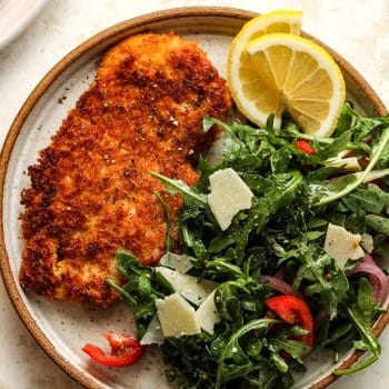 A plate with a piece of panko encrusted chicken cutlet plus an arugula salad.