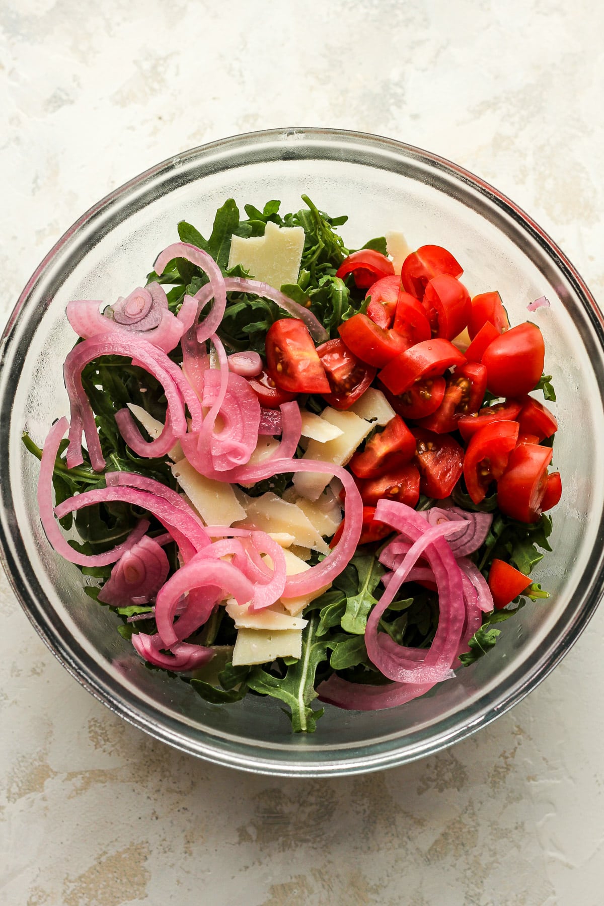 A bowl of arugula salad with tomatoes and pickled red onions.