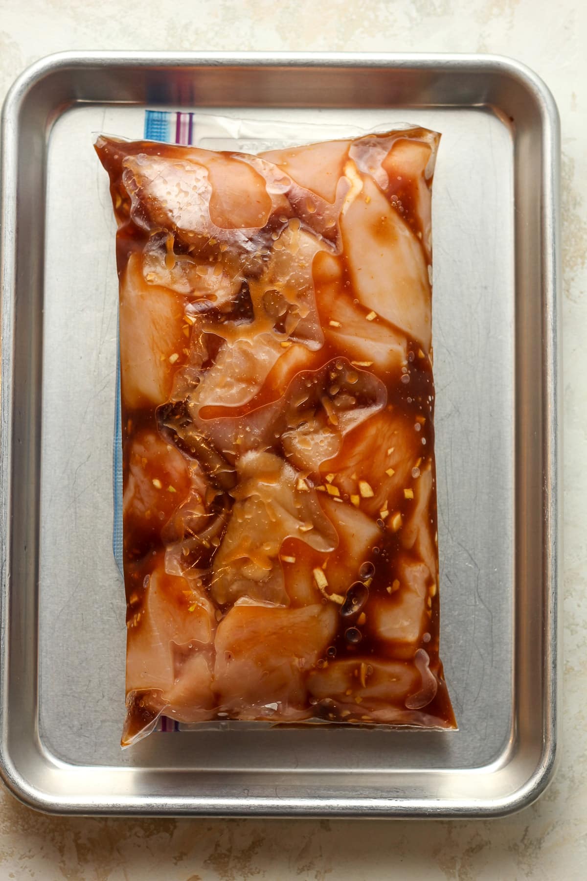 A pan with a bag of marinated chicken cubes.