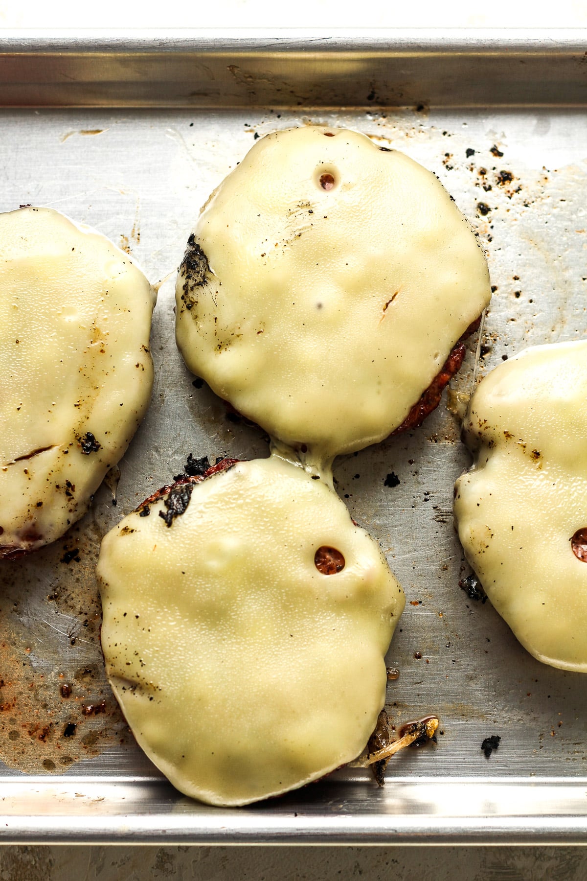 A pan of four grilled burgers with swiss cheese.