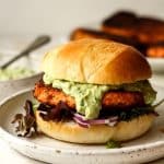 Side view of a blackened salmon burger on a homemade bun with crema and lettuce plus onion.