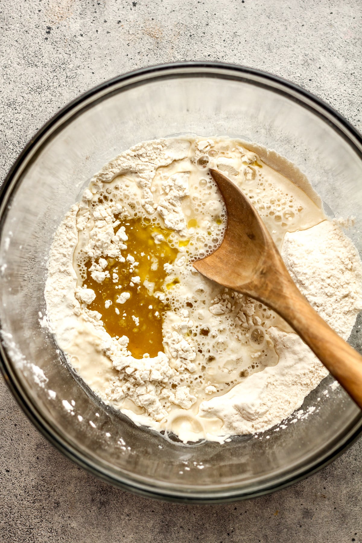 A bowl of the dry ingredients plus the olive oil and warm water, plus a wooden spoon.
