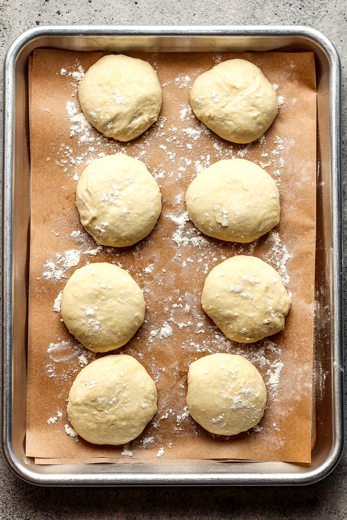 Eight round sections of tortilla dough on a sheet pan.