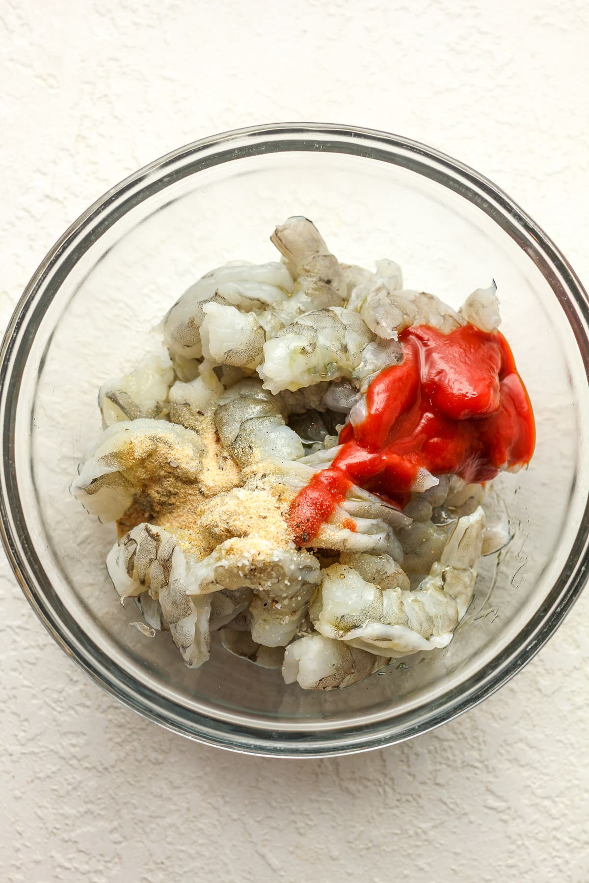 A bowl of the raw shrimp plus the sriracha, olive oil, and seasonings on top.