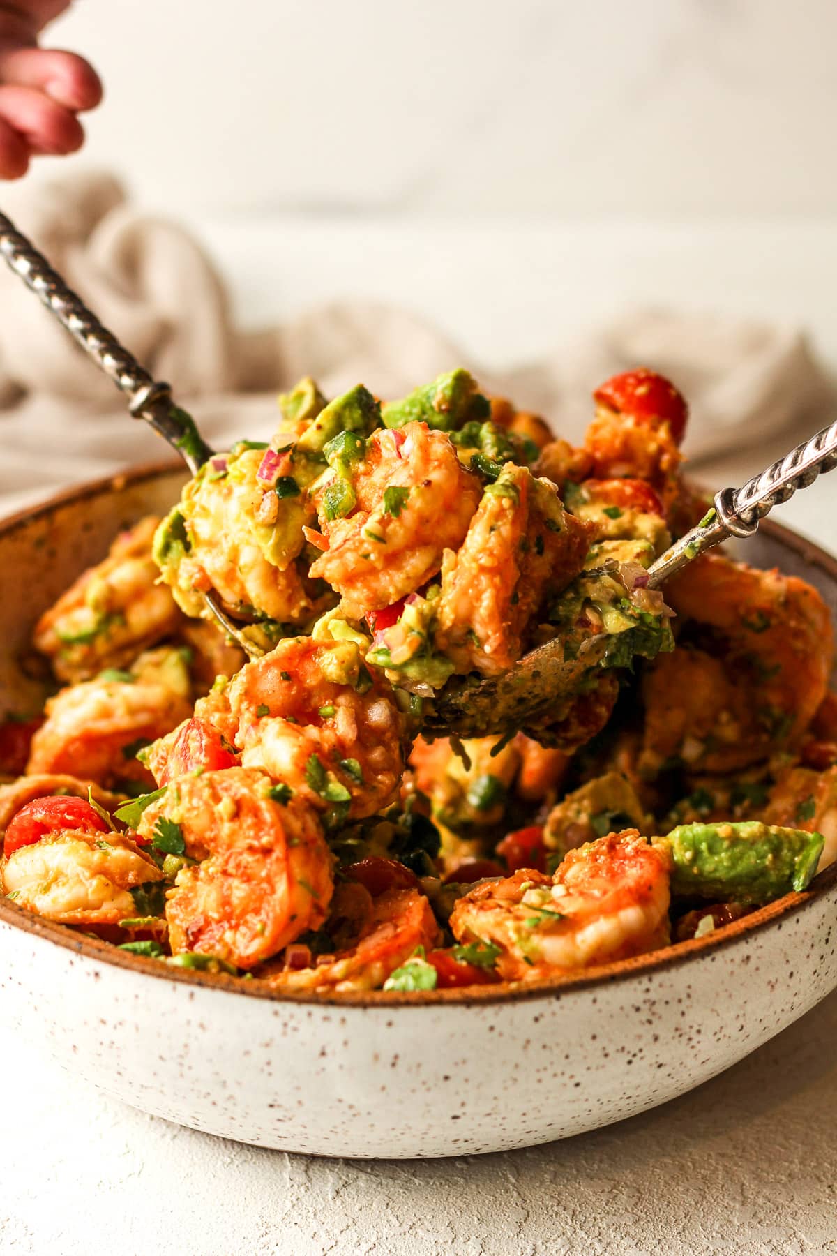 Two hands using spoons to lift up some of the Mexican shrimp salad.