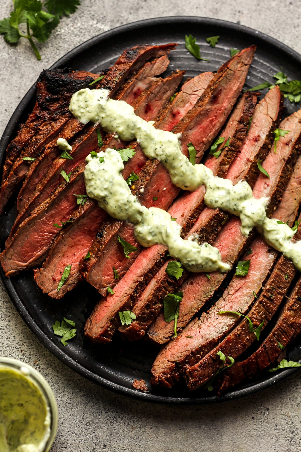 Overhead view of a plate of grilled carne asada with cilantro and crema.