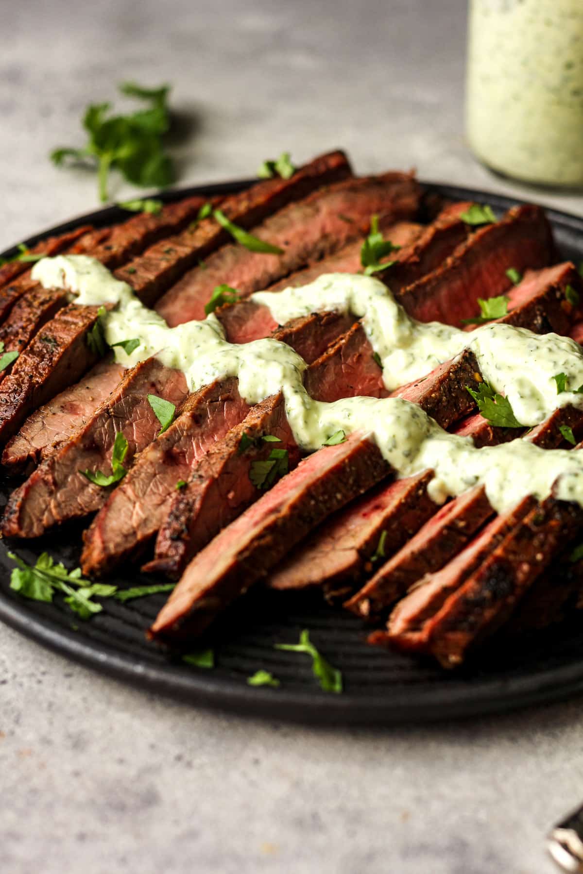 Side view of a black plate with carne asada sliced into strips with cilantro crema.