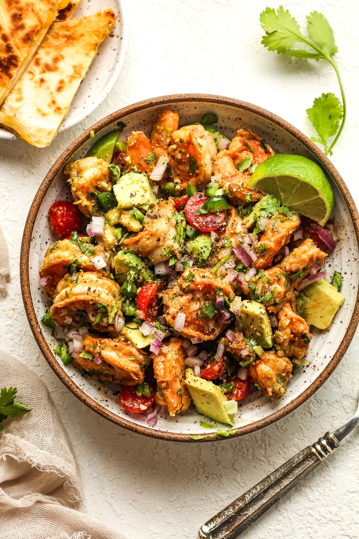 A serving bowl of the Mexican shrimp salad with a lime wedge.