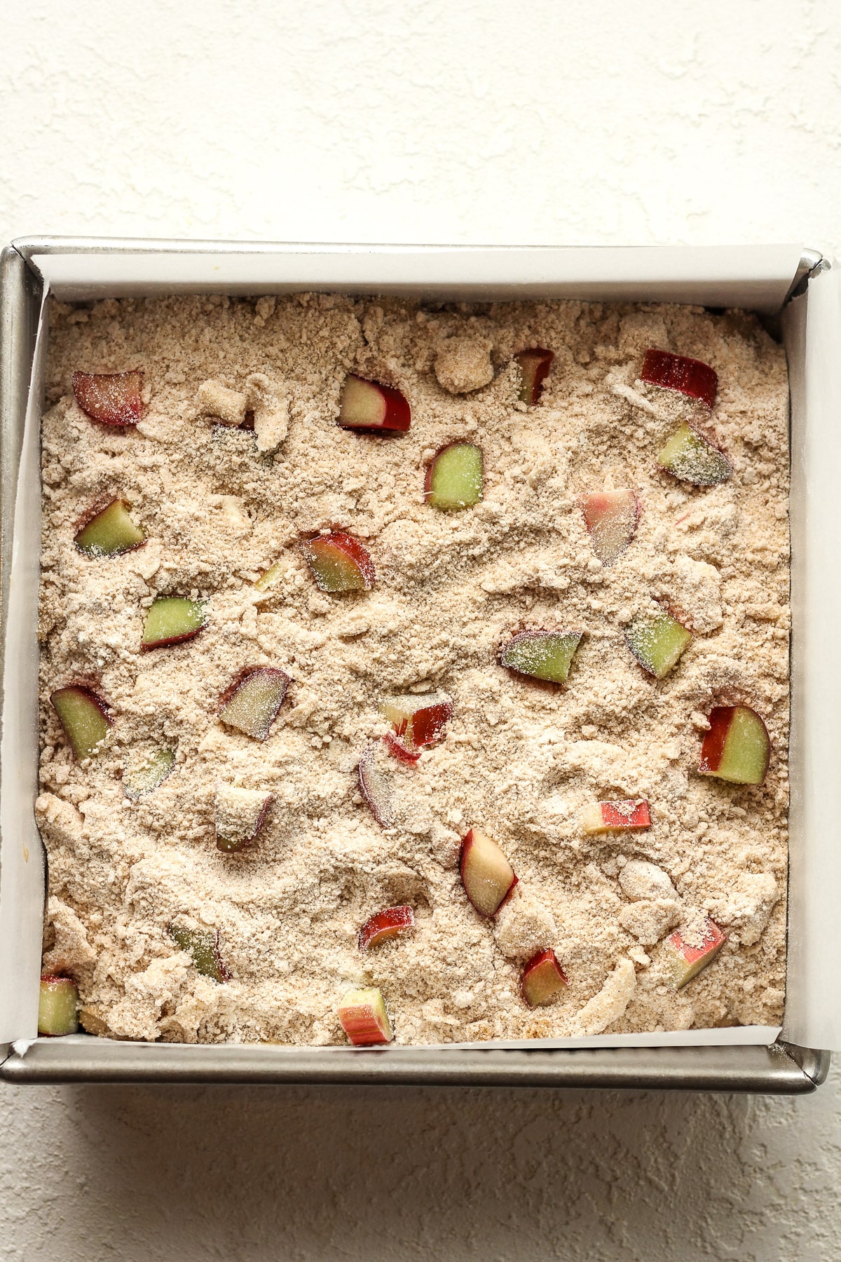 A square cake pan of the rhubarb cake after adding the streusel on top.