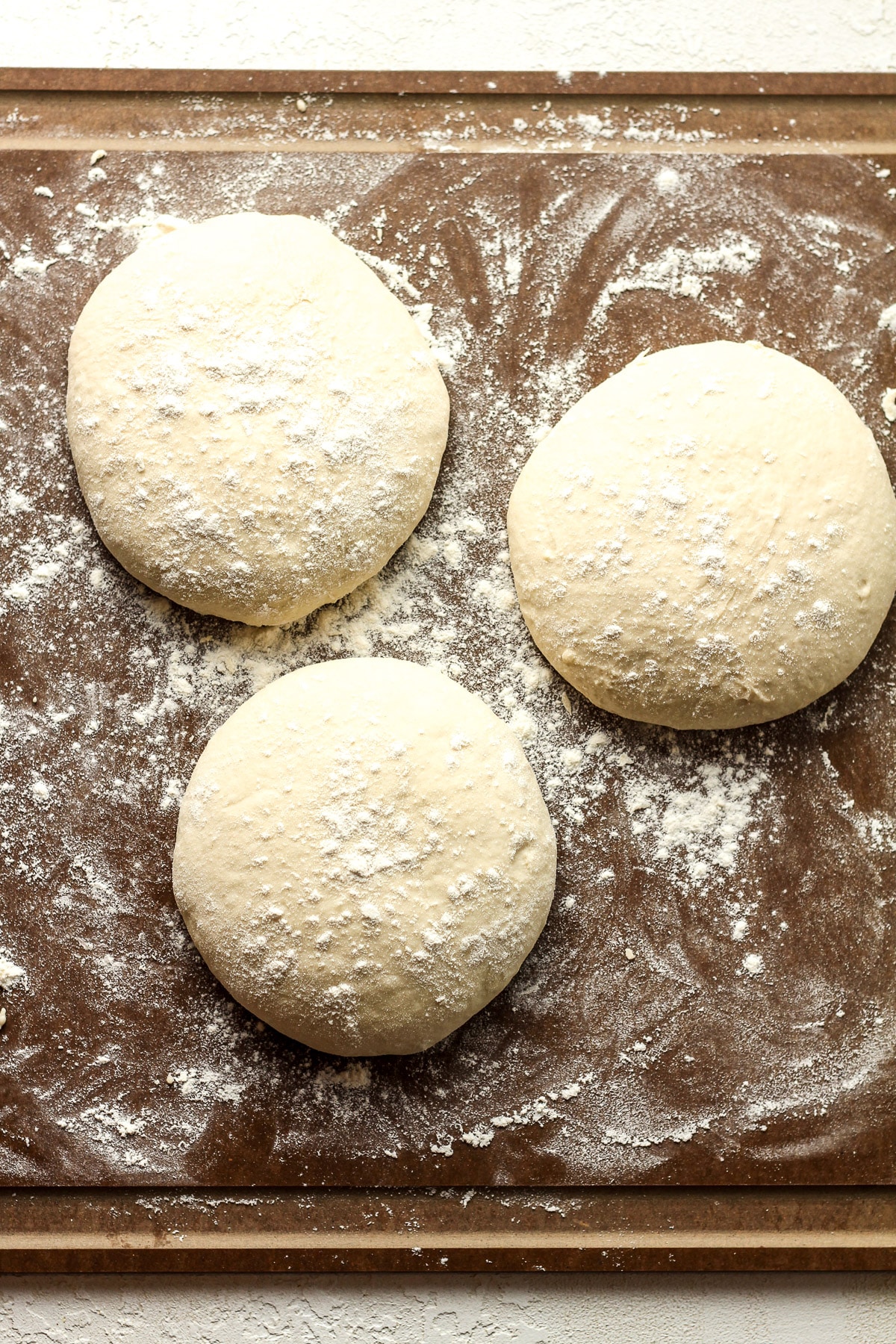 A floured board with three rounds of sourdough discard pizza dough.