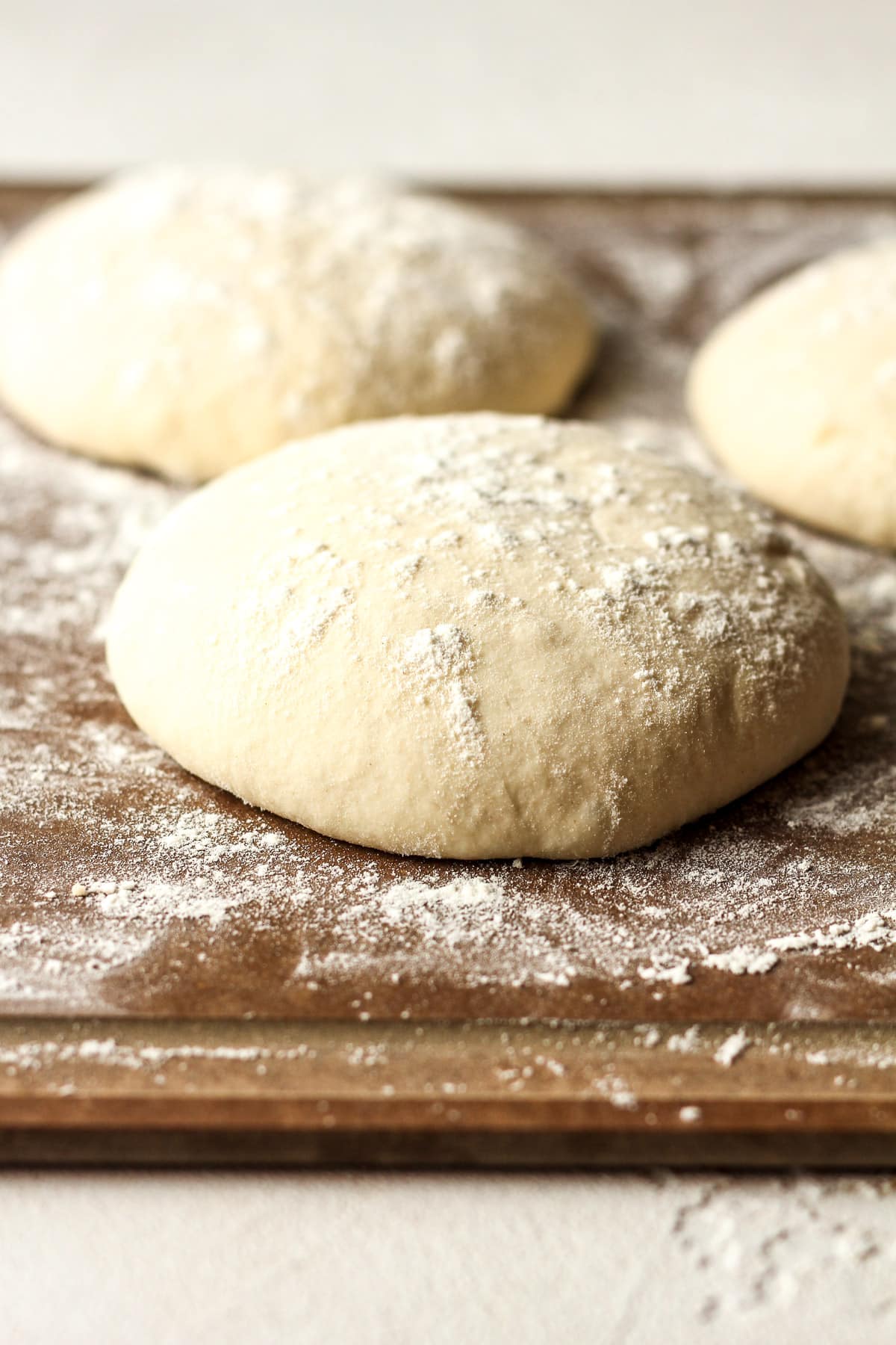 Side view of three round of sourdough pizza dough with flour sprinkled on top.