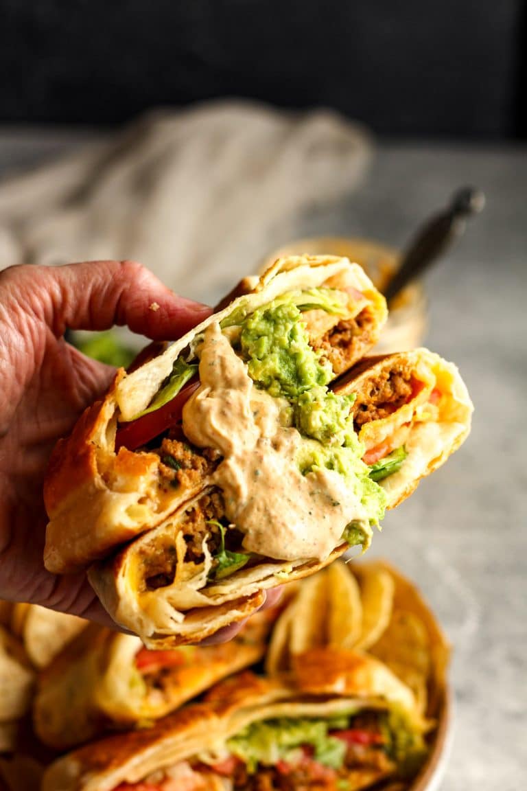 A hand holding two halves of a taco crunch wrap with chipotle dressing.