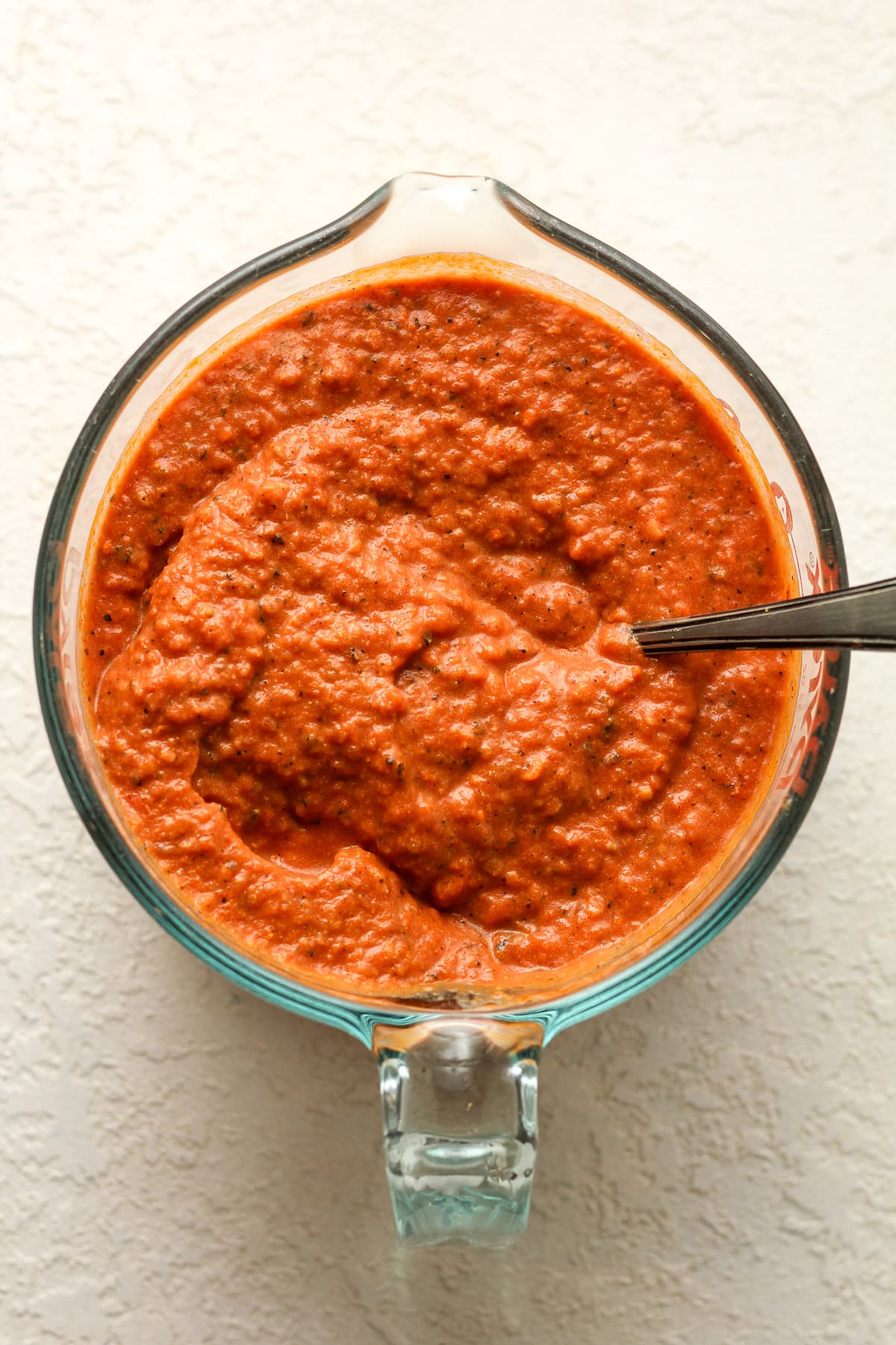 Overhead view of vodka pizza sauce in a four-cup measuring cup and a spoon.