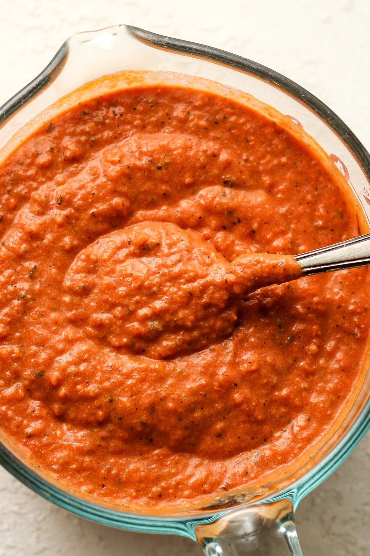 Closeup on a measuring cup of vodka pizza sauce with a spoon.